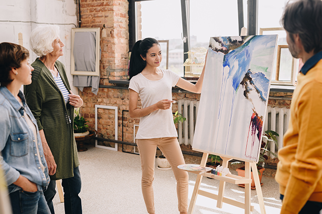 Woman presenting modern watercolor painting to audience in gallery